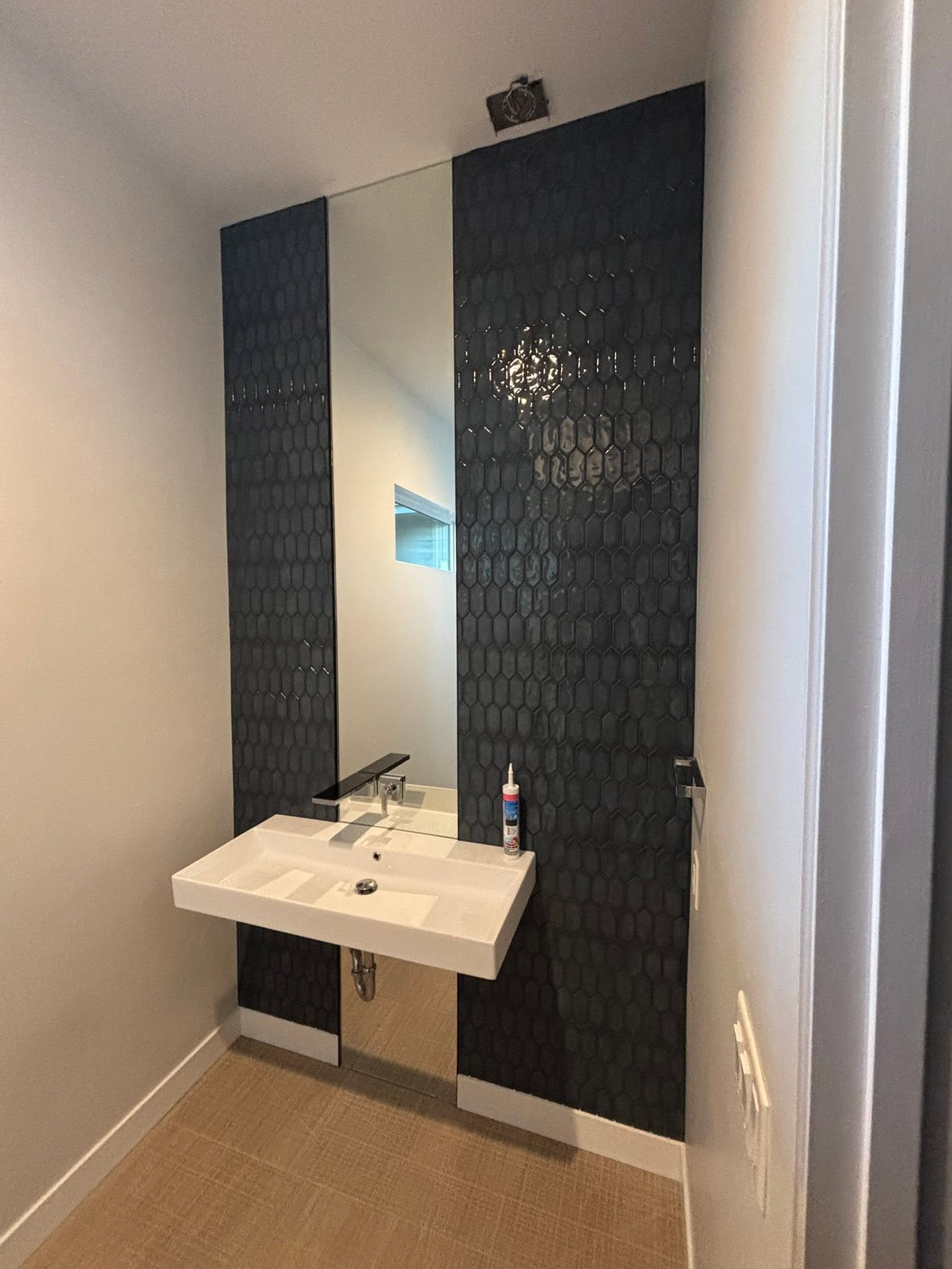 Powder room with black hexagon tile accent wall, floating sink, and full-height mirror